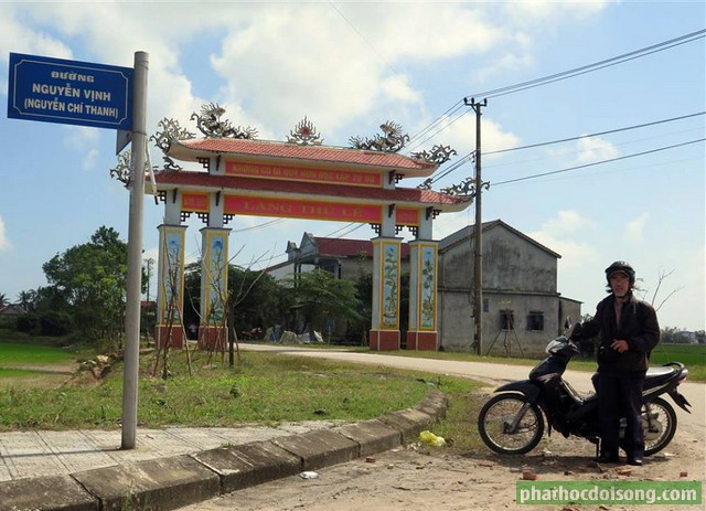 Tác giả Vĩnh Khánh đứng trước cổng làng Thủ Lễ